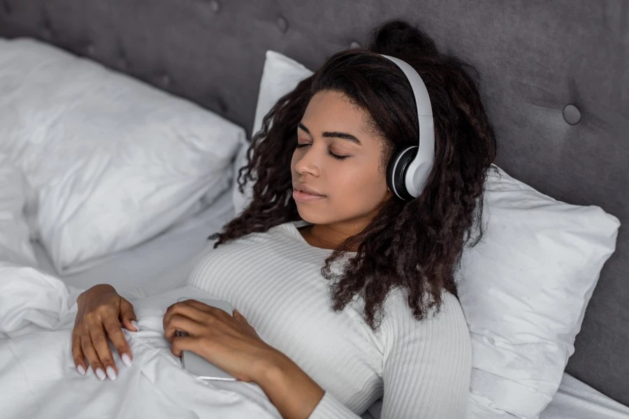 Woman lying in bed and listening to an audio with her headphones