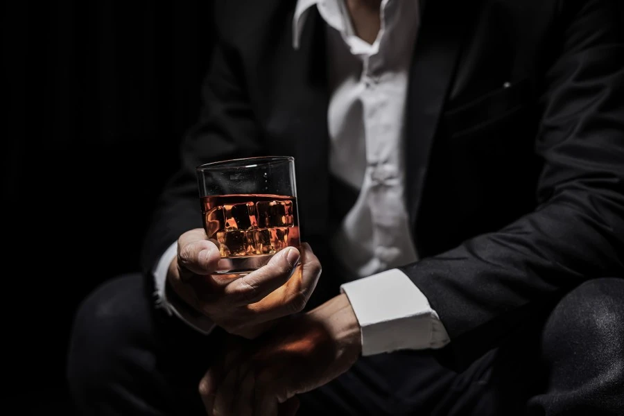 Close up of a man in a suit sitting and holding his glass of whiskey 