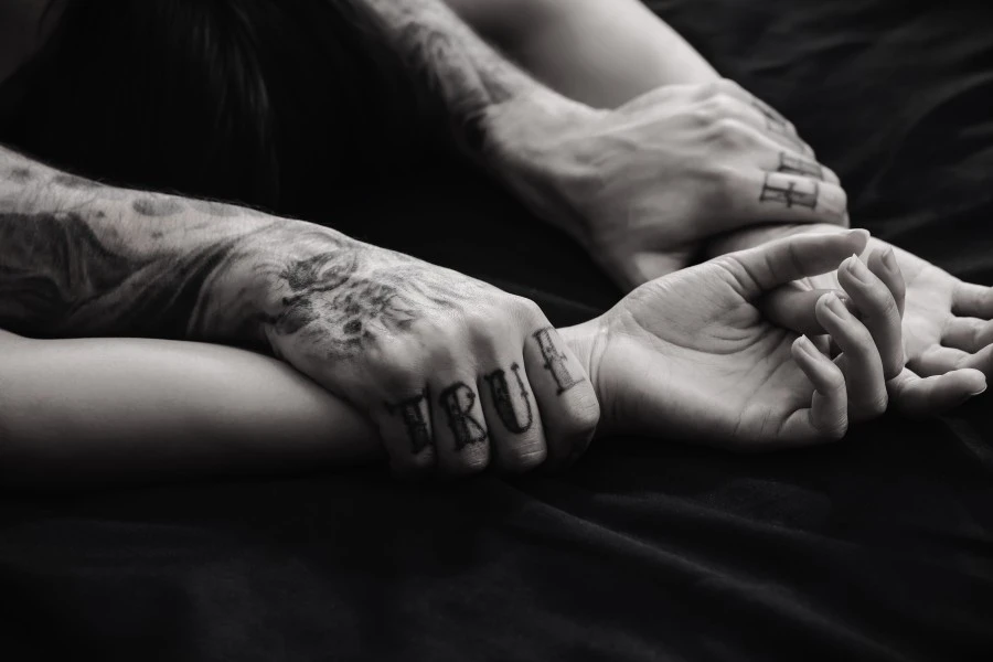 Man's hands consensually holding woman's hands above her head in bed.